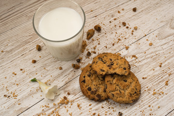 Top view of chocolate chip cookies, crumbs and a glass of milk on a wooden table