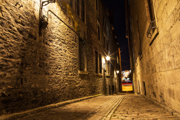 Fototapeta na wymiar Small street and historical buildings in the historic site of Old Port from Montreal, night view. Scenic background of Canadian history. Old urban architecture of Montreal culture patrimony.