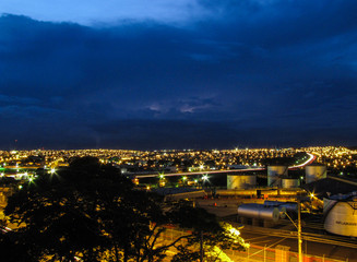 Obraz premium Foto noturna da cidade de Bauru/SP, com céu nublado iluminado por relâmpagos antes da chuva, capturando a atmosfera dramática de uma tempestade iminente