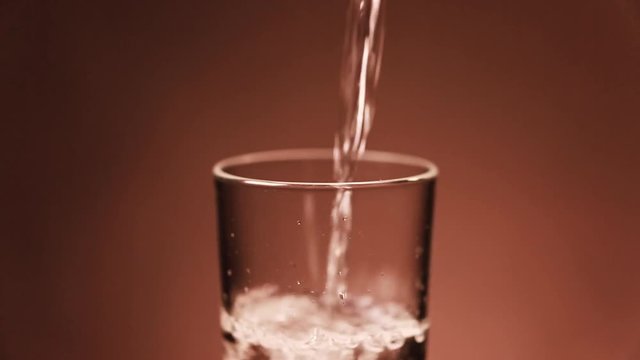 Real time pouring of cold water into a transparent glass in a warm ambient temperature with the resulting phases of the condensation process forming drops of water at the outside of the glass
