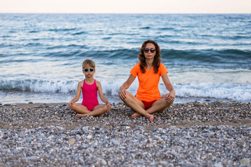 Fototapeta na wymiar Mom and daughter meditate on the beach, free space.