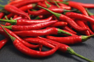 Fotobehang A lot of sharp hot spice red chilli cayenne pepper with wet drops of freshness water dew on a black graphite slate stone surface. Natural vegeterian diet organic vegetable. Dark food foto © Наталия Чубакова