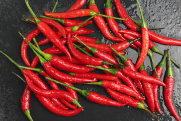 A lot of sharp hot spice red chilli cayenne pepper with wet drops of freshness water dew on a black graphite slate stone surface. Natural vegeterian diet organic vegetable. Dark food foto