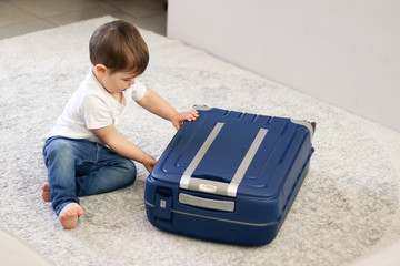 Cute little baby boy closing blue suitcase finished packing for vacation. Getting ready for...