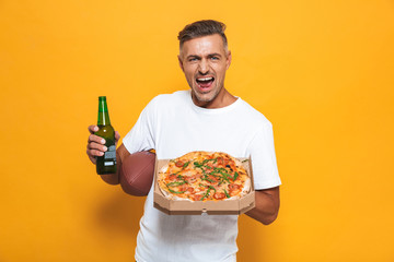 Image of positive man 30s in white t-shirt drinking beer and eating pizza while standing isolated