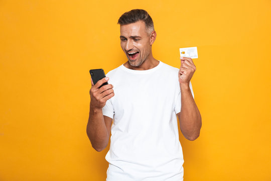 Image of bearded guy 30s in white t-shirt holding mobile phone and credit card