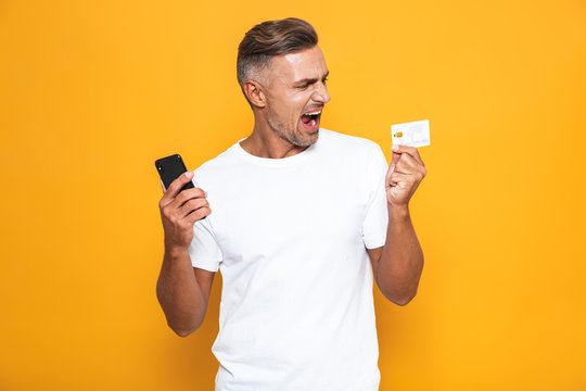 Image of caucasian guy 30s in white t-shirt holding mobile phone and credit card