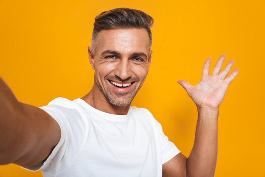 Image of optimistic man 30s in white t-shirt smiling and taking selfie photo
