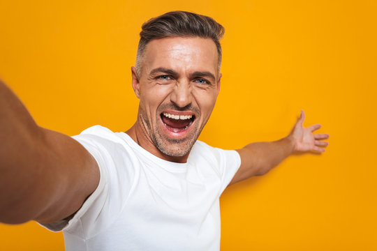 Image of cheerful man 30s in white t-shirt smiling and taking selfie photo