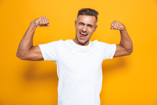 Image of strong man 30s in white t-shirt raising arms and showing biceps