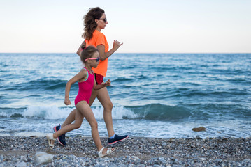 Active lifestyle: mom and daughter run along the beach.