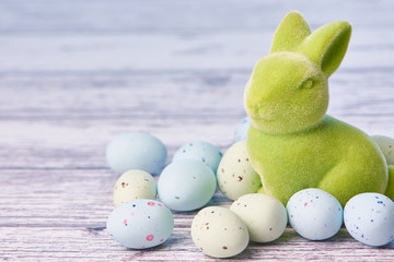 green easter bunny figure beside dragee eggs on a white wooden background with copy space