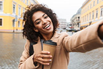 Fototapeta premium Cheerful young african woman wearing coat walking