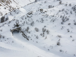 Aerial view of tunnel with snow covered road in winter landscape in Swiss mountains.