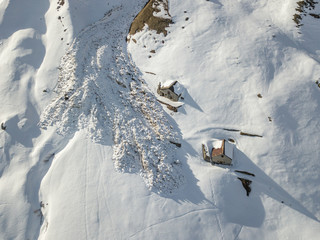 Aerial view of snow avalanche on mountain slope. Wet snow in spring sliding downhill.