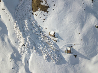 Aerial view of snow avalanche on mountain slope. Wet snow in spring sliding downhill.