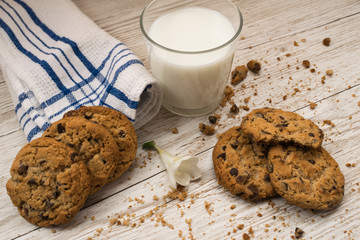 chocolate chip cookies next to a glass of milk, crumbs and a napkin on a wooden table