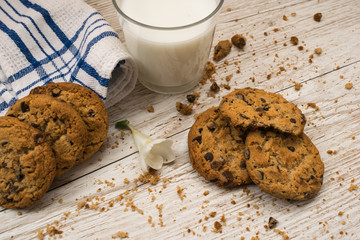 chocolate chip cookies next to a glass of milk, crumbs and a napkin on a wooden table