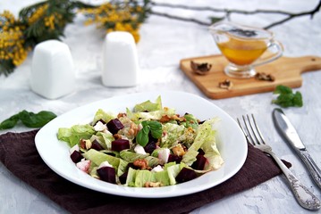 Green salad with boiled beetroot, feta and walnuts in a white plate on a gray concrete background. Seasoned with olive oil, grain mustard and vinegar. Healthy food.