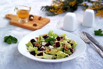 Green salad with boiled beetroot, feta and walnuts in a white plate on a gray concrete background. Seasoned with olive oil, grain mustard and vinegar. Healthy food.