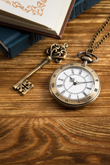 Vintage pocket watch clock with key and book on wooden background