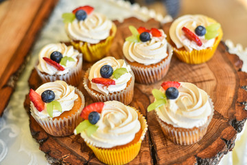 Cupcakes for happy valentine's day. On wooden brown tray. Sweet cream with strawberries and blueberries