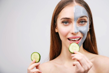 Young woman with facial mask, biting on a cucumber, spa concept