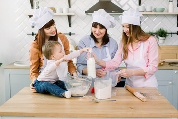 Fototapeta premium A little baby is helping her mom, aunt and grandmother knead some dough to make bread. A little baby girl opens the milk. Family cooking, Mother's Day, Baking together
