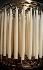 Many white wax candles hanging in bulk candlewicks to dry in a commercial candle-making production factory - Tools and process of making a traditional candle