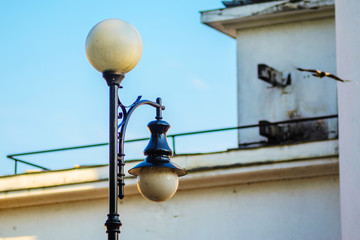 Old Black Street Lamp with White Round Plafonds Against Blue Sky and Building Facade