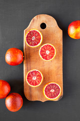 Whole and halved blood oranges on rustic wooden board on black background, top view. Flat lay,...