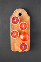 Whole and halved blood oranges on rustic wooden board over black surface, top view. Flat lay,...