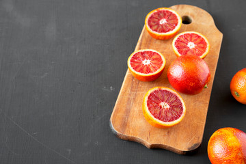 Whole and halved blood oranges on black surface, low angle view. Copy space.