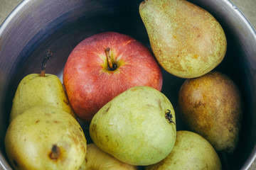 Green pears and red apple in a steel pan. 
