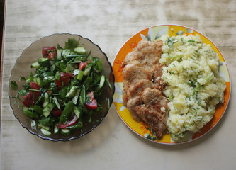 Dish consisting of fried meat and boiled potatoes and cucumber salad with green onions and tomatoes.