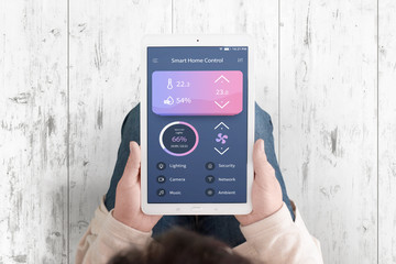 Smart home control concept app on teblet in woman hands. Flat design interface. Top view. White wooden floor in background.