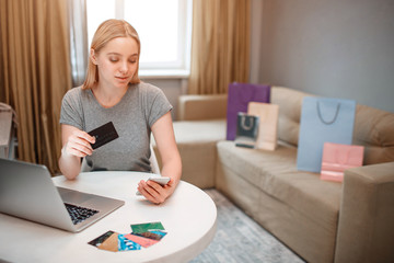 Fototapeta na wymiar Online shopping at home. Young blonde shopper with laptop and credit card is paying in online shop while sitting at the table