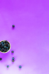 fresh organic blueberries in white bowl, some berries around on empty light violet background for copy space and design, Vertical, Top View