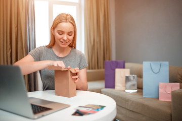Online shopping at home. Young smiling shopper is unboxing her parcel, ordered by internet, while sitting at the table