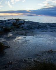 Obraz premium Ice in an interesting pattern on rocks overlooking the ocean, with an island in the distance and colorful sky during a sunset. Intentionally dark to create a moody photograph.