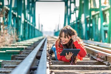 Beautiful Young Woman Lying Down on Train Tracks Using Digital Tablet.