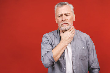 Fototapeta premium Senior aged man having sore throat and touching his neck, wearing a casual clothing isolated against red background. Hard to swallow.