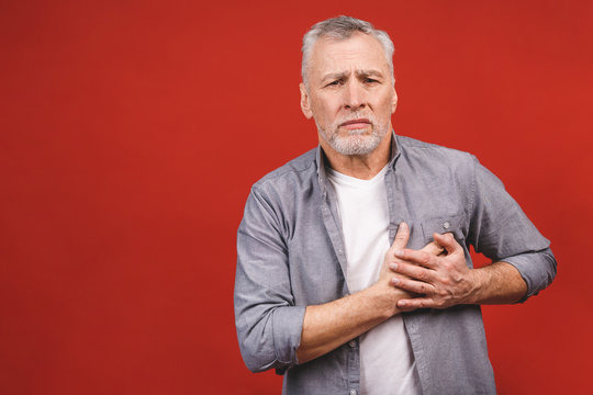 Seniour aged man having chest pain isolated against red background. Health lifestyle concept.