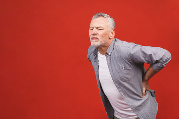 Oh, i need a massage! Portrait of a senior aged man having a back pain against a red background.