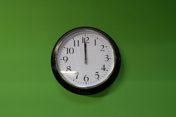 Clock isolated 1 minute before 12 o'clock or 12pm or 12am on a green wall