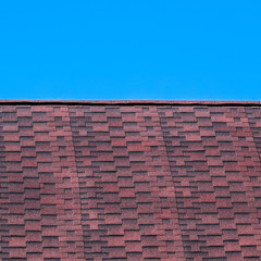 Roof from multi-colored bituminous shingles. Patterned bitumen shingles. Bituminous burgundy roof.