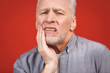 Senior aged man suffering from toothache on red background.