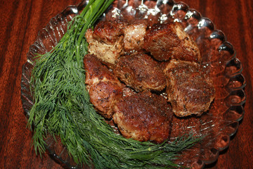 Grilled meat on the glass plate with pine branches in the background.