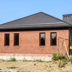 The house with plastic windows and a roof of corrugated sheet. Brown roof and brown brick