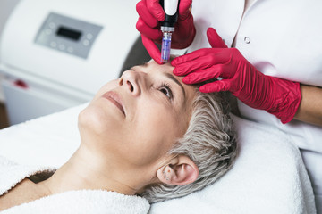 Beautiful senior woman face during facial treatment at luxury beauty clinic.
